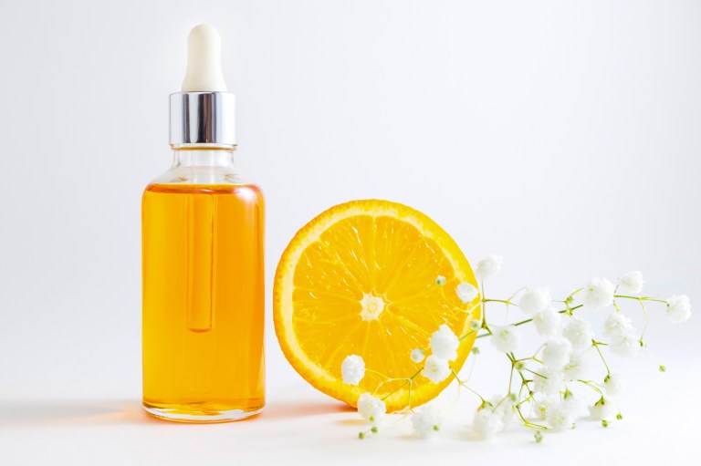 Vitamin C serum in cosmetic bottle with dropper sliced orange and flowers on white background
